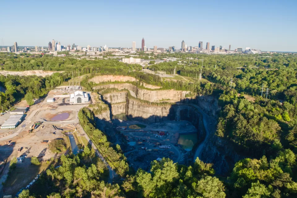 A massive hole in the ground, the Bellwood Quarry, is pictured with Downtown Atlanta rising above the horizon in the background.